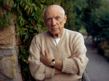 MOUGINS, FRANCE - 1966 : Pablo Picasso standing by a green fern with folded arms, wearing