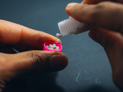 A young adult person placing colorful pills onto his fingers while seated at a table