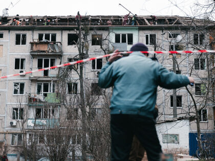 A man lifts the red and white tape cordoning off the struck residential building while oth