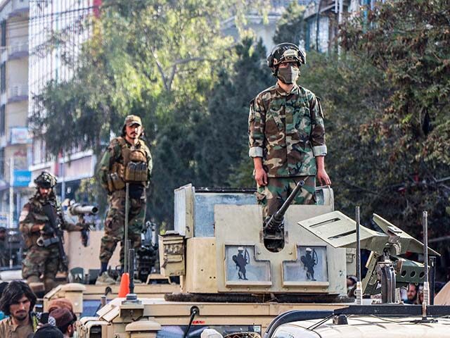GettyImages2240448261 Taliban security personnel stand over military vehicles as Afghan men gather in their supp
