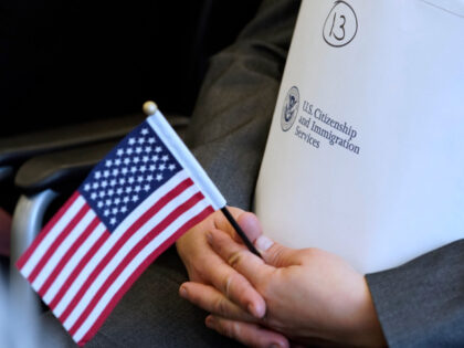 Limit Legal Immigration An applicant holds an American flag and a packet while waiting to take the oath to become