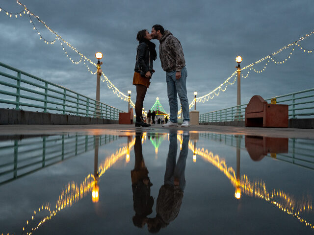 MANHATTAN BEACH, CALIFORNIA - DECEMBER 23: A couple kiss while posing for a photo along th