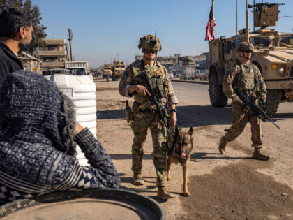 A US soldier holds a dog as forces patrol in Syria's northeastern city Qamishli, in t