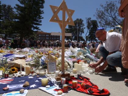 A mourner lights candles as people gather around floral tributes outside Bondi Pavilion in
