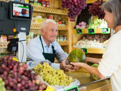 Senior salesman standing at counter in greengrocer and serving woman customer who purchasi