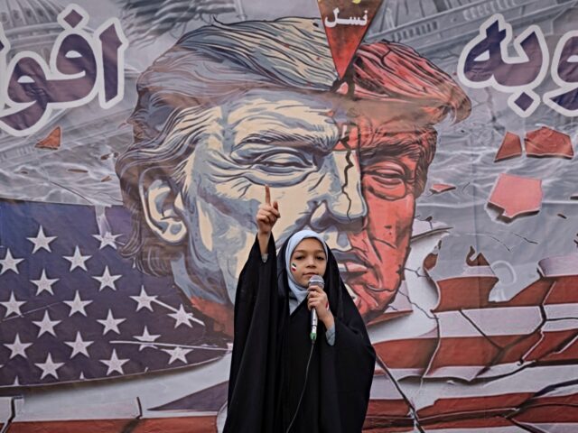 A veiled Iranian schoolgirl gestures while performing in front of an anti-U.S. banner duri