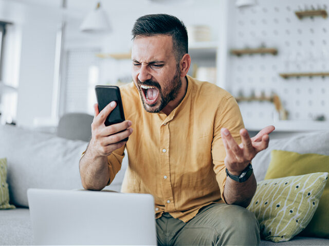 Portrait of angry businessman working on laptop and using smart phone at home.