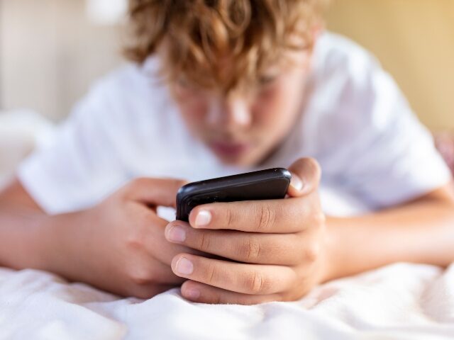 teen stares at his phone in bed
