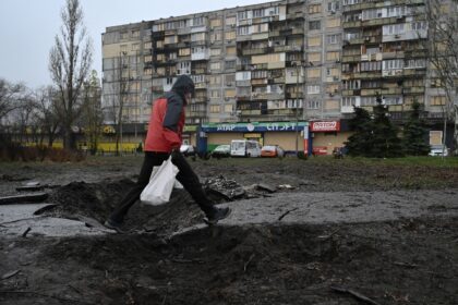 A man walks over a crater in front of a residential building damaged after a recent air at