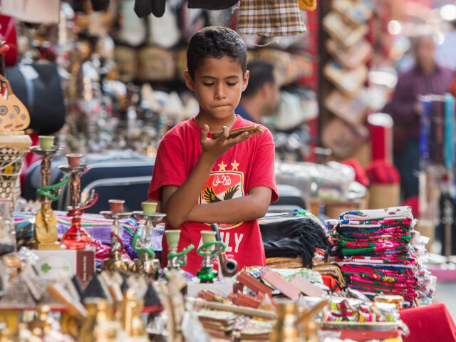 Egyptian child with cellphone in bazaar Cairo, Egypt. Young Egyptian boy looking at a cell phone in a shop selling ornate hookahs