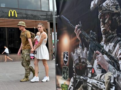TOPSHOT - A Ukrainian serviceman and his partner carrying a baby walk past a recruiting po