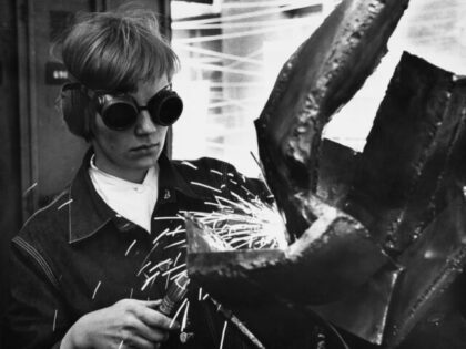 A person wearing welding goggles as they use a welding torch to construct an abstract scul
