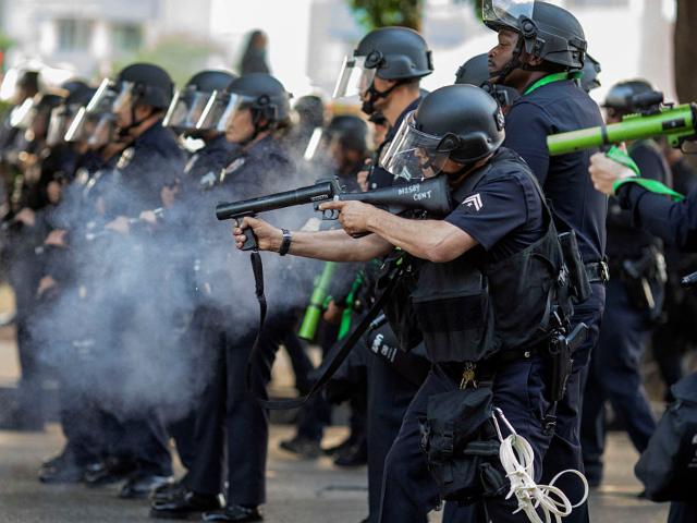 A police officer in riot gear fires a nonlethal weapon toward protesters during a demonstr