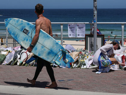 A surfer walks past floral tributes left at the promenade of Bondi Beach in Sydney on Dece