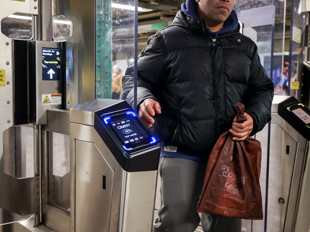A commuter exits through a turnstile past a One Metro New York (OMNY) device at a subway s