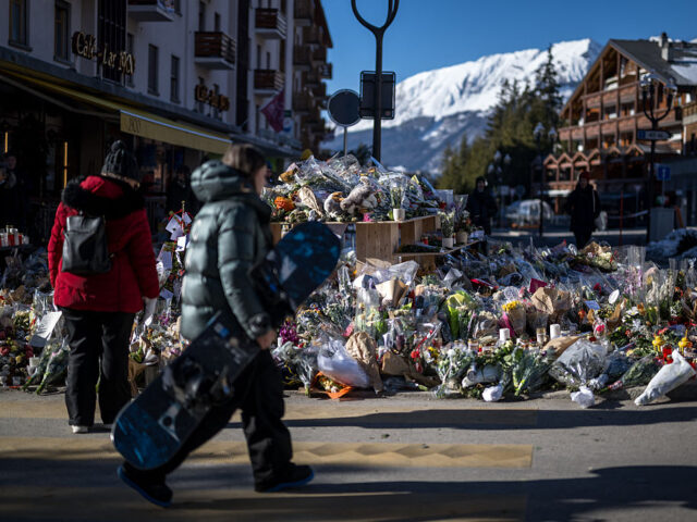 A young snowboarder walks past a makeshift memorial with laying flowers, candles and messa