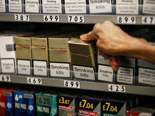 "Smoking Kills" and other warning labels sit on boxes of cigarettes as a shopkee