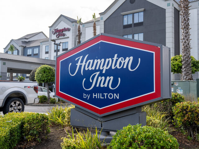 Hampton Inn by Hilton sign in front of hotel exterior with palm trees, landscaping, and pa