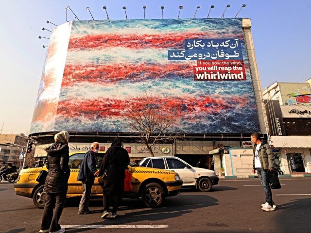 Commuters walk past an anti-US billboard installed on a building at the Enqelab Square in
