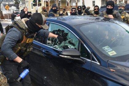 A federal officer breaks a car window to begin the process of removing a woman from her ve