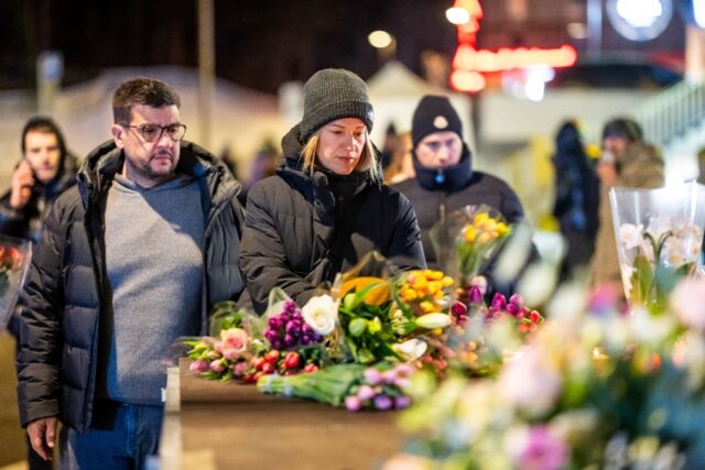 Mourners gather in front of flowers and candles laid near the site where a fire ripped thr