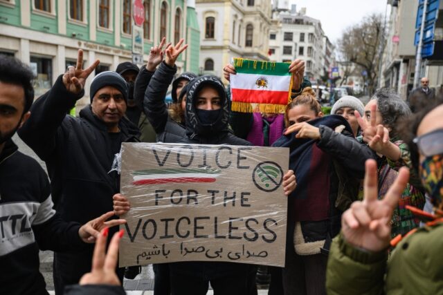 Protesters hold a placard reading 'Voice for the voiceless' and the flag of Iran