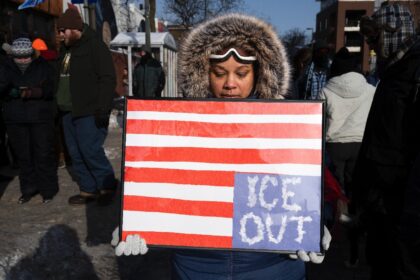 A woman holds a placard with an upside down American flag to protest violence by the ICE i