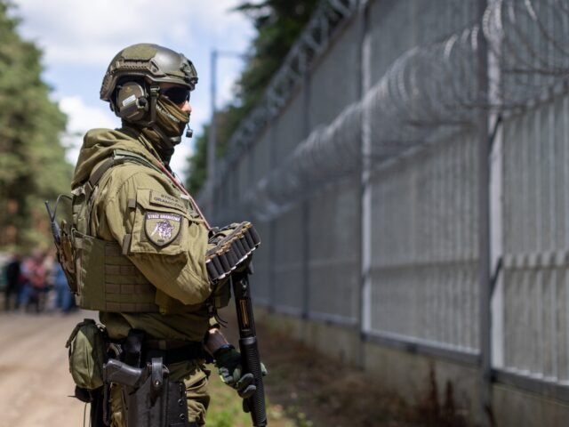 A Polish border guard officer stands at the Polish-Belarusian country border in front of t