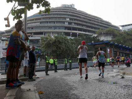 Runners pass by the 'El Helicoide' building, headquarters of the Bolivarian National Intel