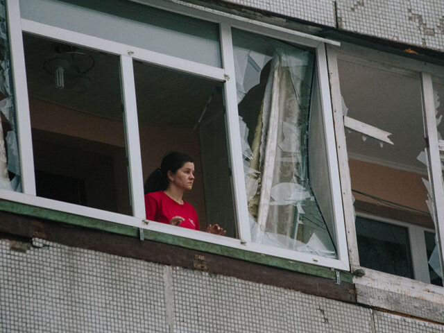 A resident of a building damaged by a Shahed attack looks out of a shattered window in Kha
