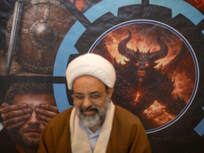 An Iranian cleric smiles as he sits in front of a banner depicting a symbolic image of the