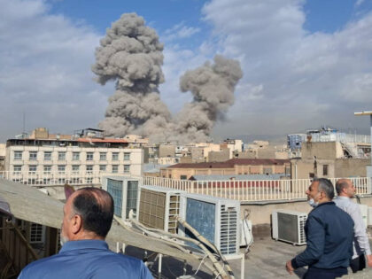 People watch as smoke rises on the skyline after an explosion in Tehran, Iran, Saturday, F