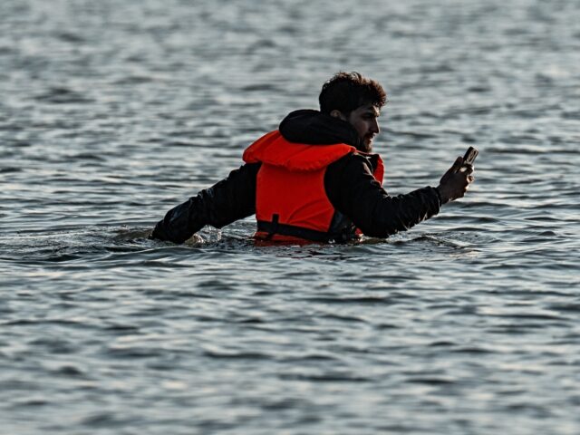 GRAVELINES, FRANCE - JUNE 17: A man looks at his phone as he wades in water to board a mig