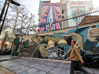 An Iranian man walks past an anti-US and anti-Israel banner hanging on a building in Pales