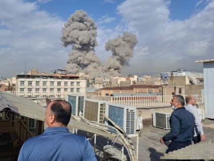 People watch as smoke rises on the skyline after an explosion in Tehran, Iran, Saturday, F
