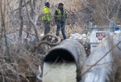Emergency workers look on as raw sewage flows out of a drainage pipe into the C&O Cana