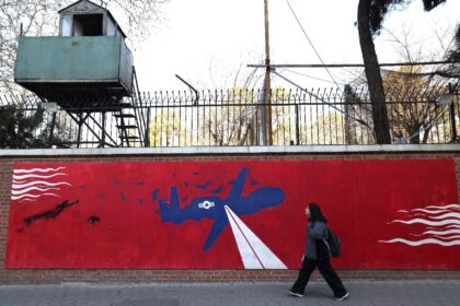 A woman walks past a mural depicting a US drone painted on the outer walls of the former U