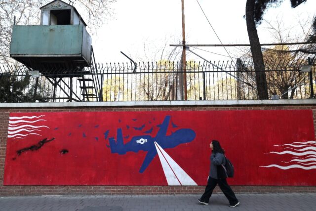 A woman walks past a mural depicting a US drone painted on the outer walls of the former U