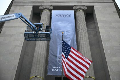 Workers on an aerial lift watch after installing a new banner featuring an image of US Pre