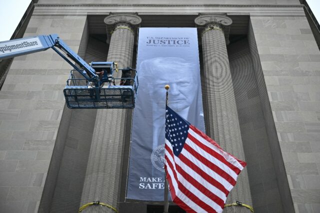 Workers on an aerial lift watch after installing a new banner featuring an image of US Pre