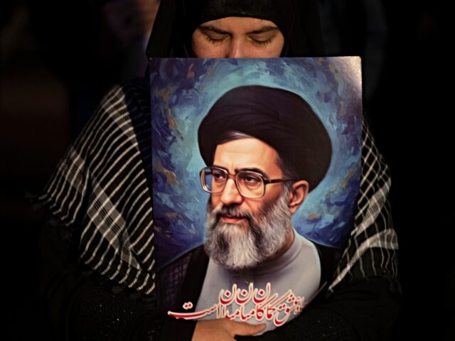 An Iranian woman holds a portrait of Iran's Supreme Leader Ayatollah Ali Khamenei while pa
