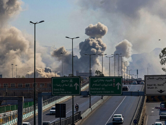 TOPSHOT - Motorists drive along an expressway as plumes of smoke rise after a strike in Te