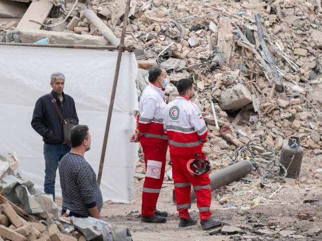 Two members of the Iranian Red Crescent Society stand on the ruins of buildings in a resid