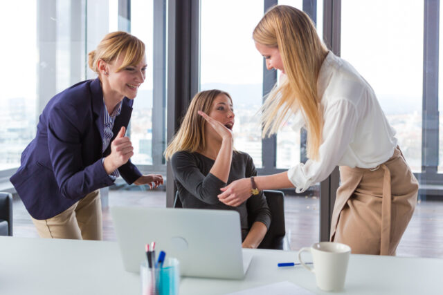 Three business women in modern office celebrating good project results.