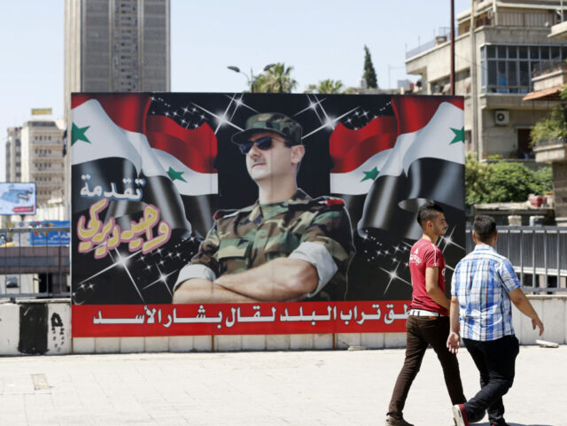 Syrian youths walk past a billboard showing a picture of Syrian President Bashar al-Assad