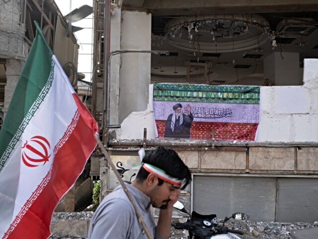 An Iranian man carries a national flag and walks past a banner depicting a portrait of Ira