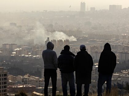 TEHRAN, IRAN - MARCH 2: Men watch from a hillside as a plume of smoke rises after an explo