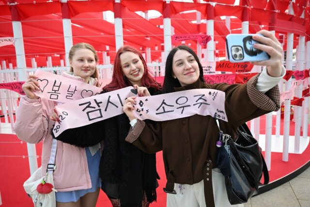 BTS fans take a selfie with banners inscribed with their love songs at a fan zone.