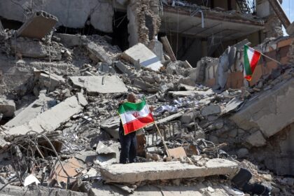 A man holds an Iranian flag amid the debris of a destroyed building following airstrikes i