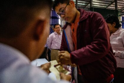 Military chief Min Aung Hlaing (back C) watches a voter ink their finger as he visits a po